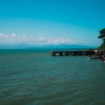 Paisagem costeira de Ilhabela, com um píer diante do mar e vegetação exuberante.