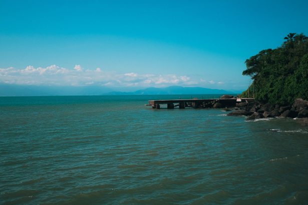 Paisagem costeira de Ilhabela, com um píer diante do mar e vegetação exuberante.