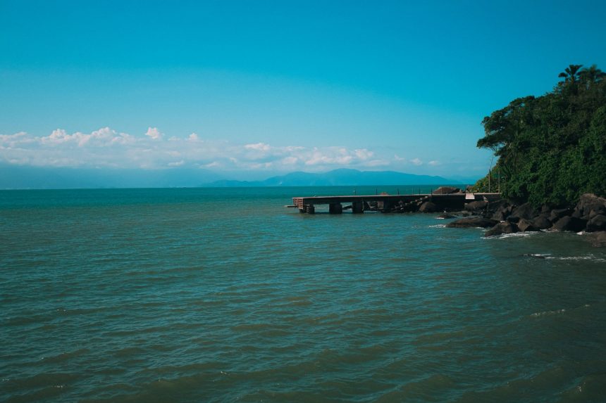 Paisagem costeira de Ilhabela, com um píer diante do mar e vegetação exuberante.