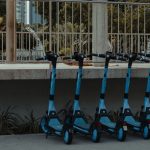 Fileira de patinetes elétricos azuis estacionados ao ar livre, representando a mobilidade urbana compartilhada.