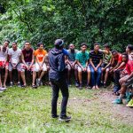 Adolescentes e adultos ouvem atentamente durante uma atividade ao ar livre em um parque