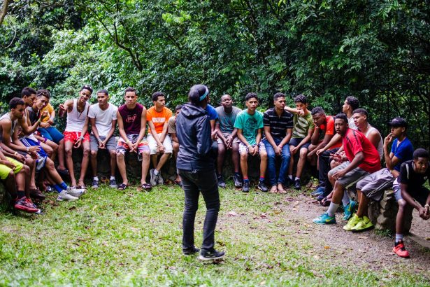 Adolescentes e adultos ouvem atentamente durante uma atividade ao ar livre em um parque