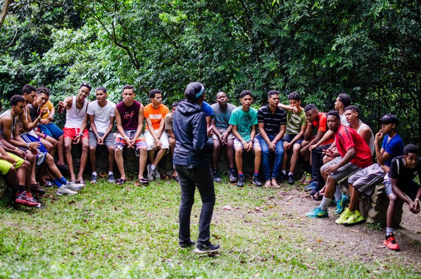 Adolescentes e adultos ouvem atentamente durante uma atividade ao ar livre em um parque