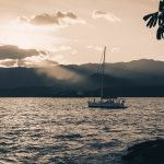 Veleiro navega ao entardecer diante das montanhas de Ilhabela, no litoral brasileiro.