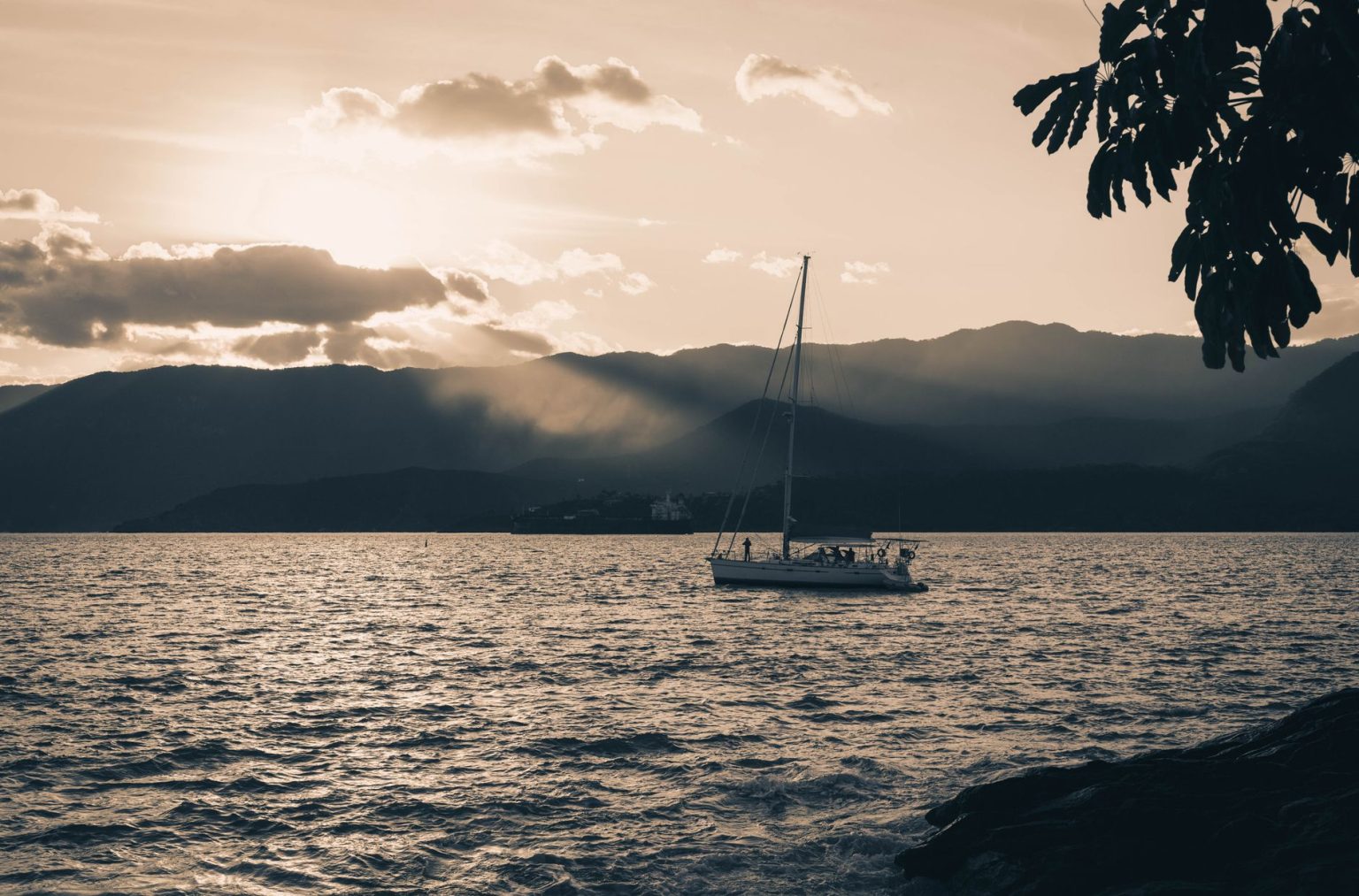 Veleiro navega ao entardecer diante das montanhas de Ilhabela, no litoral brasileiro.