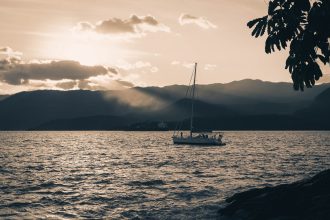 Veleiro navega ao entardecer diante das montanhas de Ilhabela, no litoral brasileiro.