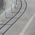 Vista aérea de uma calçada urbana com piso tátil e corrimãos de proteção.