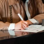 Mulher assina um documento em um balcão de atendimento administrativo.