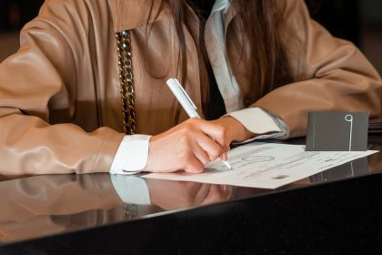 Mulher assina um documento em um balcão de atendimento administrativo.