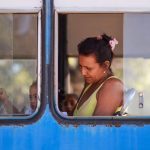 Passageira sentada dentro de um ônibus durante o trajeto, vista pela janela.