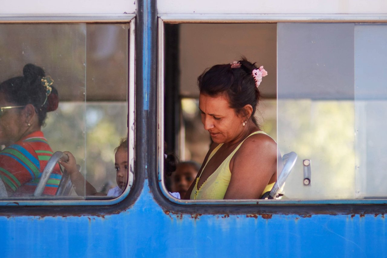 Passageira sentada dentro de um ônibus durante o trajeto, vista pela janela.