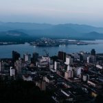 Vista aérea de uma área urbana junto a um curso d’água, com ilhas e morros ao fundo.