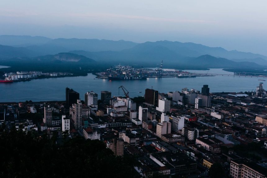 Vista aérea de uma área urbana junto a um curso d’água, com ilhas e morros ao fundo.