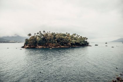 Vista costeira da Ilha das Cabras, em Ilhabela, com embarcações no mar e vegetação ao redor.
